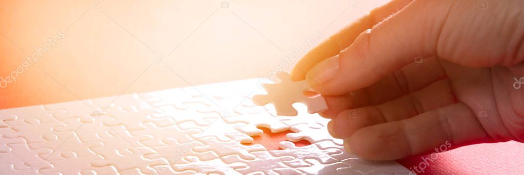 Hand inserting last missing puzzle on red background, business concept.