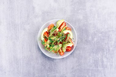 Domatesli salata, ovacado ve gri bir masada mikro yeşiller..