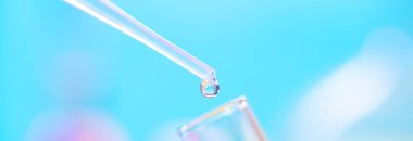 Kimyasal test tüpü ve kimyasal pipette mavi arka planda şeffaf sıvı damlası, yakın plan.