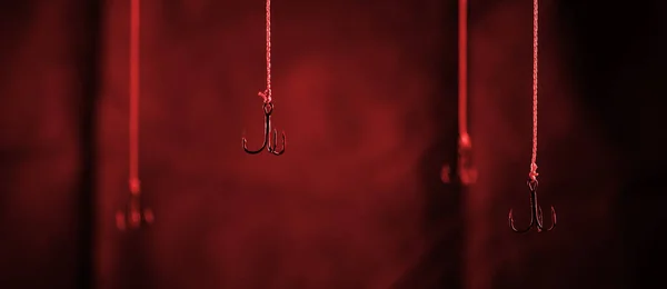 Fishing hooks hang on a dark background. Single hook in focus close-up.