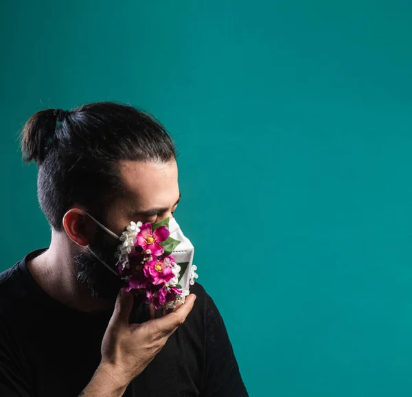 Yüzünde tıbbi maske olan Latin orta yaşlı bir adam maske altında gül çiçekleri yetişiyor oksijen eksikliği, kötü ekoloji, kirli hava ve hastalık. Adam elleriyle maske tutarken gözlerini kapatır..