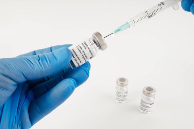 Beyaz arka planda üç adet Covid-19 aşı şişesi olan mavi eldivenler ve tıbbi uzmanlara ve risk altındaki insanlara SARS-CoV-2 aşısı yapmak için bir şırınga. Boşluğu kopyala.