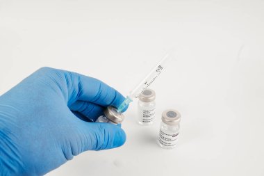 Beyaz arka planda üç adet Covid-19 aşı şişesi olan mavi eldivenler ve tıbbi uzmanlara ve risk altındaki insanlara SARS-CoV-2 aşısı yapmak için bir şırınga. Boşluğu kopyala.