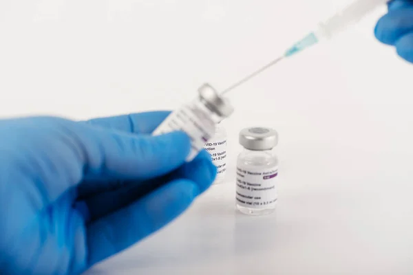 Beyaz arka planda üç adet Covid-19 aşı şişesi olan mavi eldivenler ve tıbbi uzmanlara ve risk altındaki insanlara SARS-CoV-2 aşısı yapmak için bir şırınga. Boşluğu kopyala.