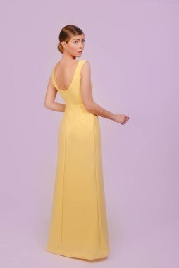 Sarı elbiseli genç bir kızın kameraya bakarken orta boy fotoğrafı. Mor arka planda izole edilmiş. Kopyalama alanı tasarla.