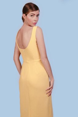 Sarı elbiseli güzel sarışın kızın kameraya bakarken çekilmiş Amerikan pozu. Mavi arka planda izole edilmiş. Kopyalama alanı tasarla.