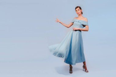 Ürününüzü sunan mavi elbiseli, şık, genç, sarışın bir Fransız kızı. Mavi arka planda izole edilmiş. Etkileyici yüz ifadeleri..