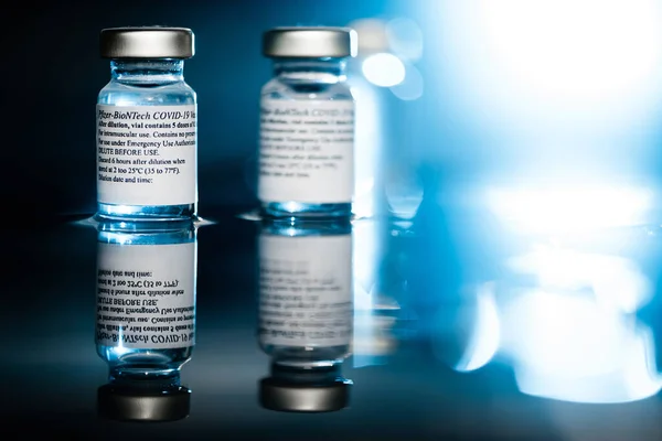 San Sebastian, Gipuzkoa, İspanya; 24 Nisan 2021. Tıbbi uzmanlara ve risk altındaki insanlara enjekte etmek için iki pfizer coronavirus şişesi. Mavi ve siyah arka plan. Mavi arka ışıklar.
