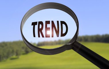 Bulanık doğa arka plan üzerinde kelime eğilim ile büyüteç. Trend kavramını arama