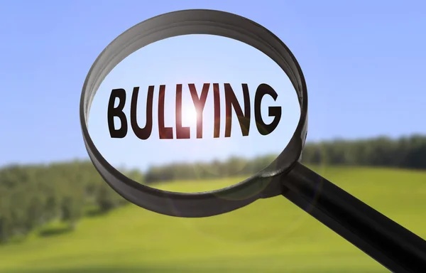 Lupa con la palabra bullying sobre fondo borroso de la naturaleza. Buscando el concepto de bullying — Foto de Stock