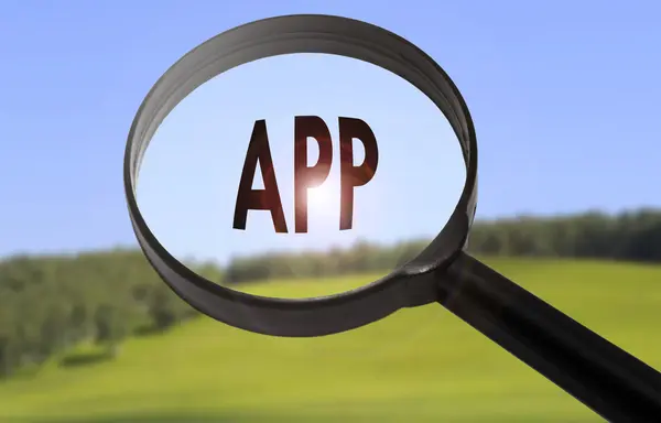 Lupa con la palabra app (aplicación) sobre fondo borroso de la naturaleza. Búsqueda de aplicación (aplicación) concepto —  Fotos de Stock