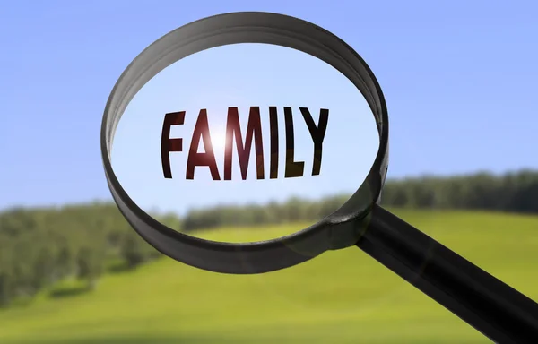 Zvětšovací sklo s rodinou slovo na pozadí rozmazané přírody. Hledání rodiny koncepce — Stock fotografie
