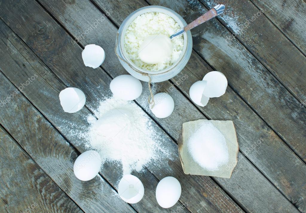 Eggs, flour, cottage cheese, sour cream, sugar and spoon on a wooden table top