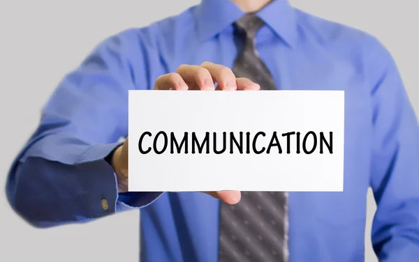 Forretningsmand i blå skjorte og grå slips viser et kort med indskriften kommunikation - Stock-foto
