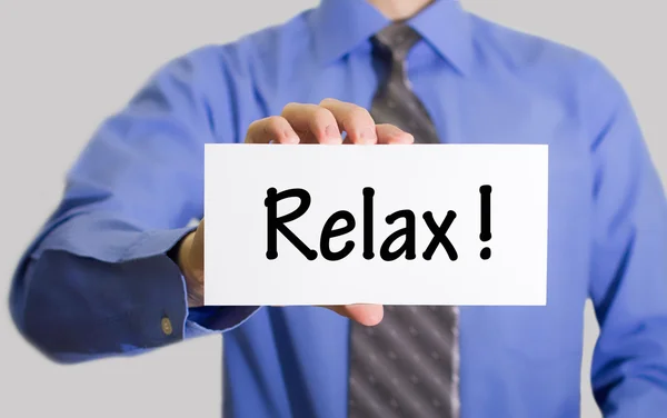 Businessman in blue shirt and gray tie shows a card with the inscription relax — Stockfoto