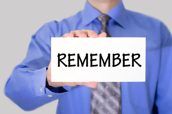 Businessman in blue shirt and gray tie shows a card with the inscription remember — 图库照片