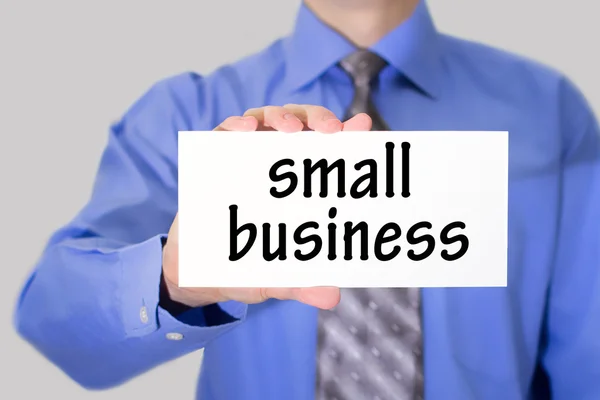 Businessman in blue shirt and gray tie shows a card with the inscription small business — ストック写真