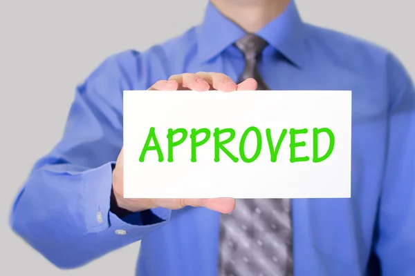 Businessman in blue shirt and gray tie shows a card with the inscription approved — Stockfoto