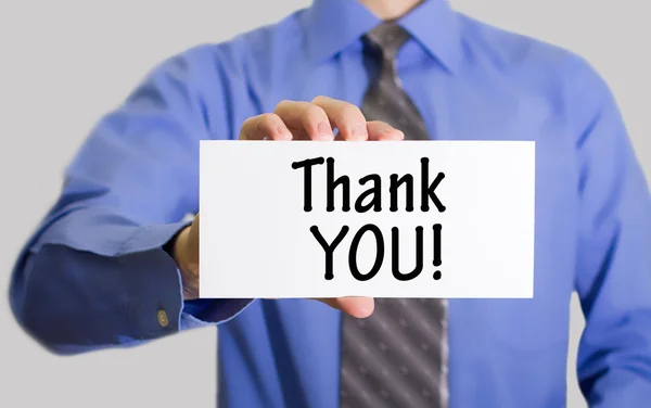 Businessman in blue shirt and gray tie shows a card with the inscription thank you!
