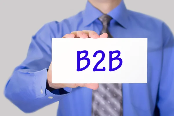 Empresario en camisa azul y corbata gris muestra una tarjeta con la inscripción b2b —  Fotos de Stock