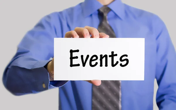 Businessman in blue shirt and gray tie shows a card with the inscription events — Stok fotoğraf