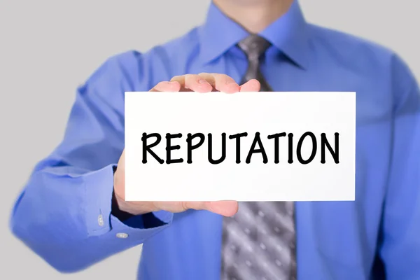 Businessman in blue shirt and gray tie shows a card with the inscription reputation — Stock Photo, Image