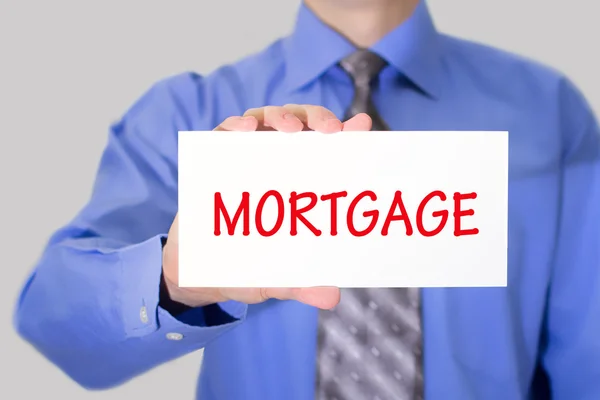 Businessman in blue shirt and gray tie shows a card with the inscription mortgage — Stockfoto