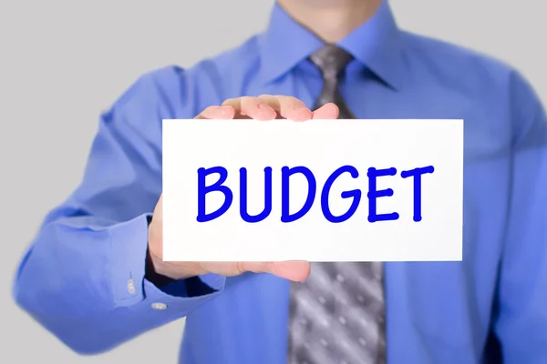 Empresario en camisa azul y corbata gris muestra una tarjeta con el presupuesto de inscripción —  Fotos de Stock
