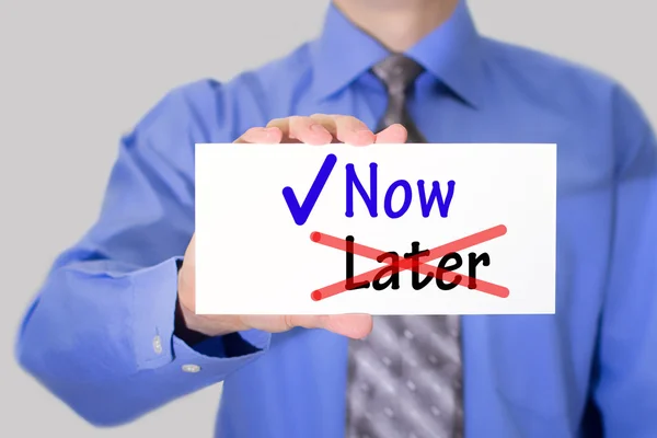 Businessman in blue shirt and gray tie shows a card with the inscription now — Stock Photo, Image