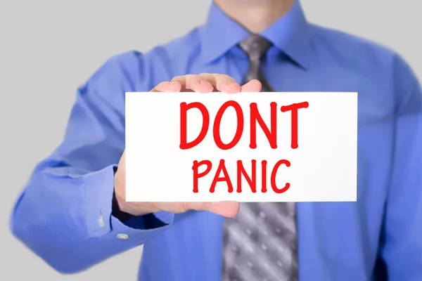 Businessman in blue shirt and gray tie shows a card with the inscription dont panic — Stock Photo, Image