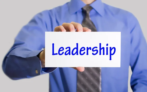 Businessman in blue shirt and gray tie shows a card with the inscription leadership. — Stock Photo, Image