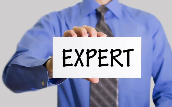 Businessman in blue shirt and gray tie shows a card with the inscription expert — Stock Photo, Image