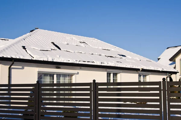 Modern black solar panels on the roof of a house in winter, covered with snow. Green energy off season concept