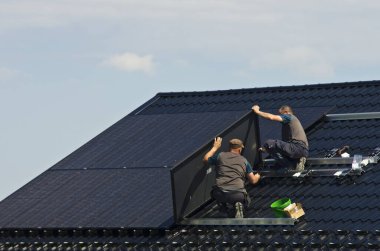 Özel bir evin metal çatısına yeni siyah güneş panelleri kurmak. Ekoloji, yenilenebilir enerji ve yeşil sürdürülebilir güç kaynağı soyut.