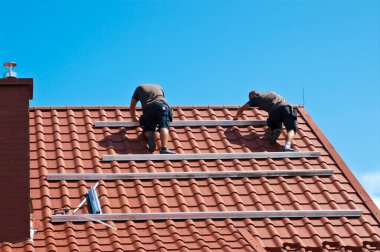 İki adam özel bir evin çatısına yeni güneş panelleri kuruyor. Yenilenebilir enerji kavramı ve yeşil enerji soyut.