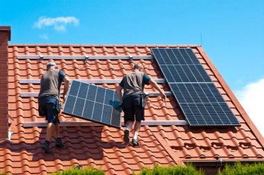 İki adam özel bir evin çatısına yeni güneş panelleri kuruyor. Yenilenebilir enerji kavramı ve yeşil enerji soyut.
