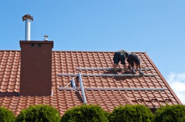 İki adam özel bir evin çatısına yeni güneş panelleri kuruyor. Yenilenebilir enerji kavramı ve yeşil enerji soyut.