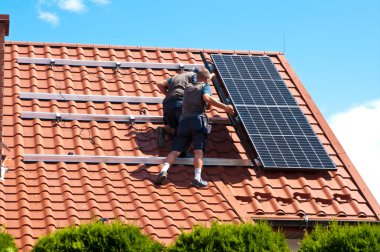İki adam özel bir evin çatısına yeni güneş panelleri kuruyor. Yenilenebilir enerji kavramı ve yeşil enerji soyut.