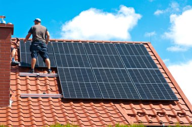 İki adam özel bir evin çatısına yeni güneş panelleri kuruyor. Yenilenebilir enerji kavramı ve yeşil enerji soyut.