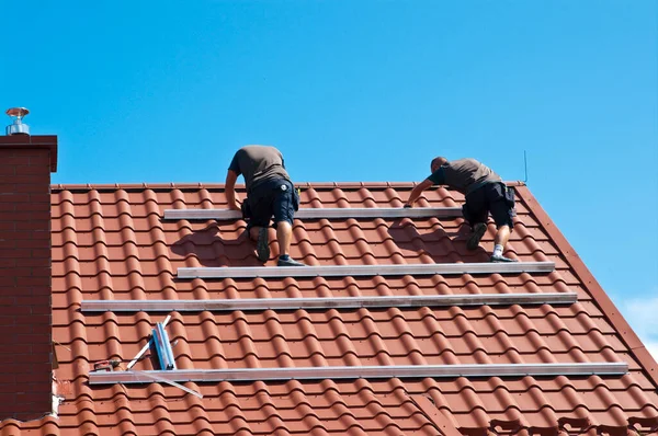 İki adam özel bir evin çatısına yeni güneş panelleri kuruyor. Yenilenebilir enerji kavramı ve yeşil enerji soyut.