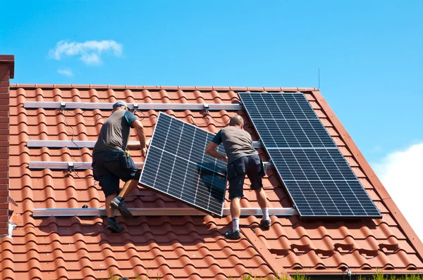 İki adam özel bir evin çatısına yeni güneş panelleri kuruyor. Yenilenebilir enerji kavramı ve yeşil enerji soyut.