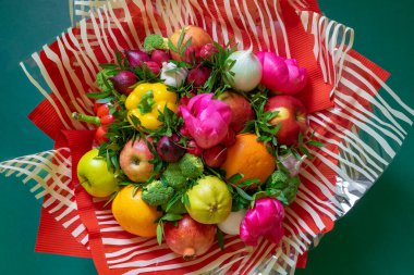 Rengarenk bir buket sebze, pembe şakayık ve kıvrımlı kırmızı kağıda sarılı yeşil yapraklı meyve ve yemyeşil renkli çizgili selofan. Sağlıklı beslenme kavramı.