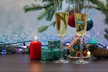 İki bardak köpüklü şampanya. Renkli bir ev şeklinde Noel zencefilli ekmeği. Kırmızı yanan bir mumla Noel süslemesi.