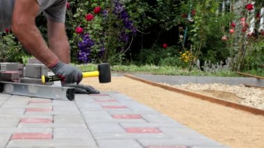 Bir inşaat işçisi, bir kır evinin avlusuna kaldırımlar için beton bloklar kuruyor..
