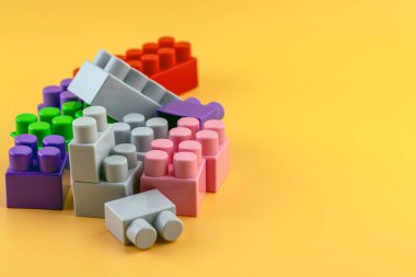 Sarı arka planda plastik figürler ve tuğlalar. Renkli plastik lego tuğlaları.