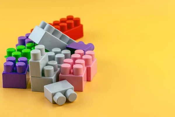 Sarı arka planda plastik figürler ve tuğlalar. Renkli plastik lego tuğlaları.