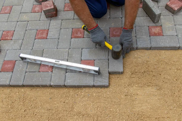 Bir inşaatçı bir kır evinin avlusuna kaldırımlar için beton bloklar kurar. Seçici odak.