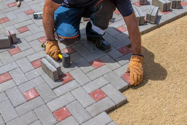 Eldivenli bir zanaatkar kaldırım taşlarını katman katman serer. Evin avlusuna kumlu bir temele gri beton döşeme döşeme..