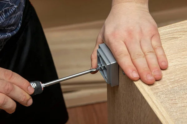 Assembling furniture, close-up of a tool in hand. The mounting screw is screwed into the hole in the board