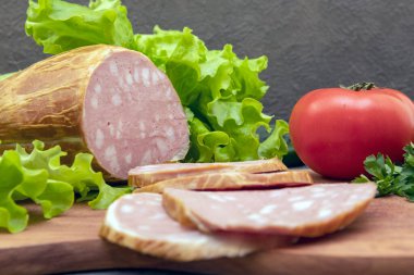 Kesme tahtasındaki geleneksel büyük dilimlenmiş sosis. Yeşil marul ve domates. Ev yapımı yemek. Üst Manzara. Yakın plan.